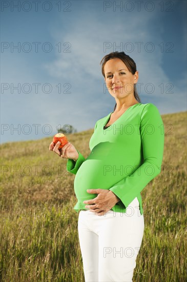 Pregnant Hispanic woman eating apple in field