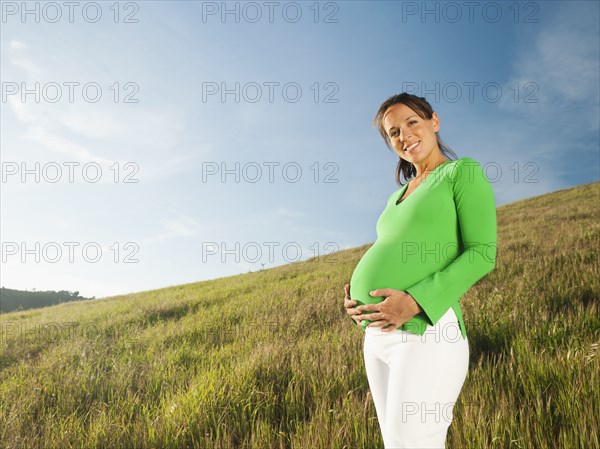 Pregnant Hispanic woman standing in field