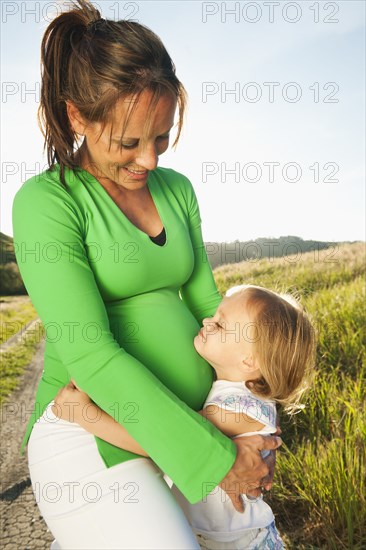 Pregnant mother hugging daughter outdoors