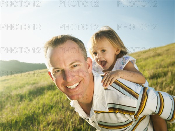 Father carrying daughter on his back in field