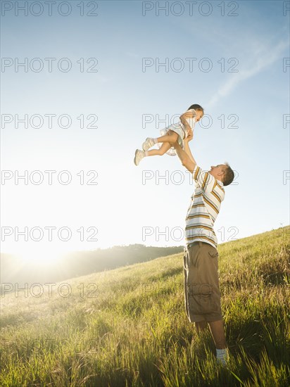 Father standing in field lifting daughter