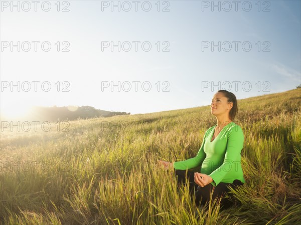 Pregnant Hispanic woman practicing  yoga in field