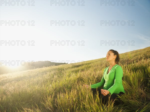 Pregnant Hispanic woman practicing  yoga in field