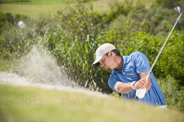 Caucasian golfer hitting ball out of bunker