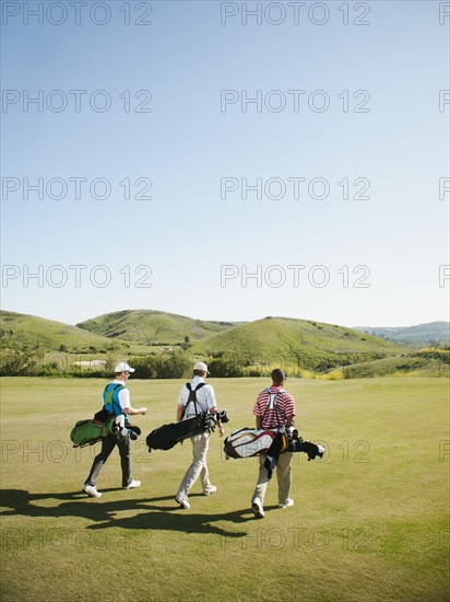 Men carrying golf bags on golf course