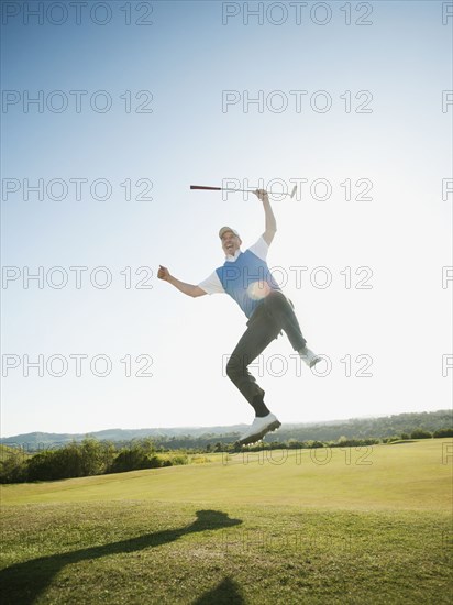 Excited Caucasian golfer jumping in mid-air on golf course