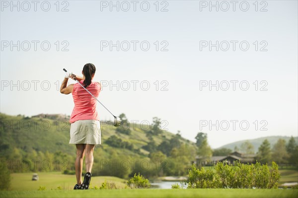 Mixed race woman swinging golf club on golf course