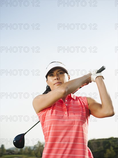 Mixed race woman swinging golf club on golf course