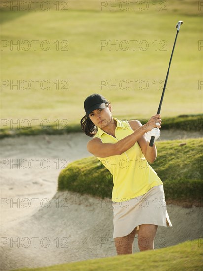 Mixed race woman hitting golf ball out of bunker