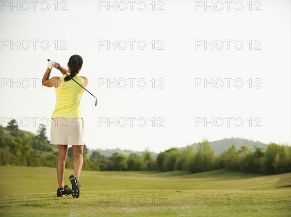 Mixed race woman swinging golf club on golf course