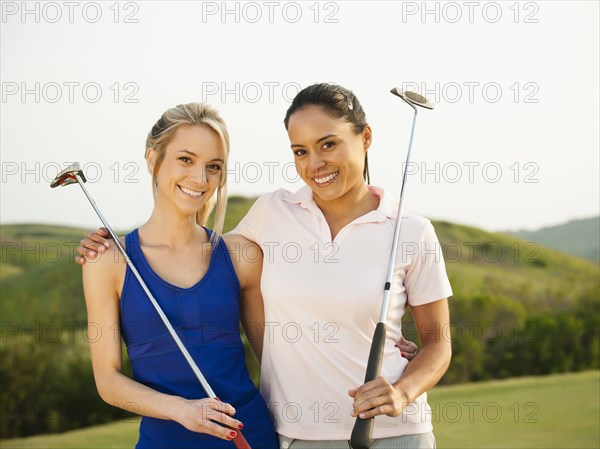 Women with golf clubs hugging on golf course