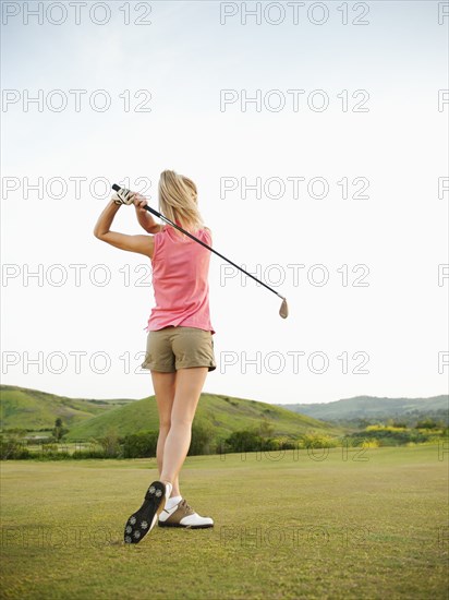 Caucasian woman swinging golf club on golf course