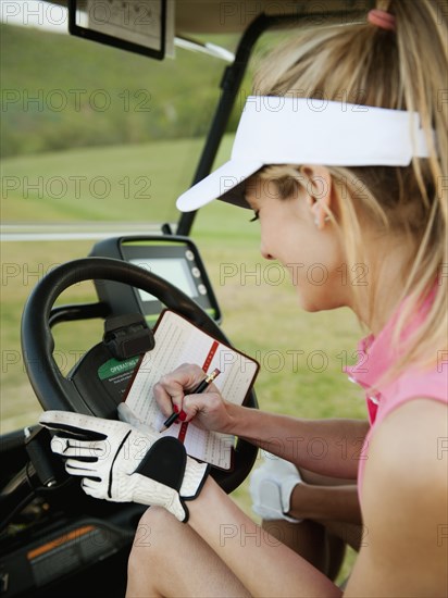 Caucasian woman in golf cart writing on score card