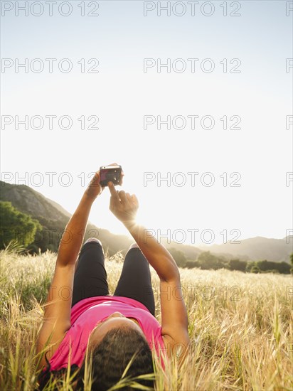 Black woman laying in field using cell phone