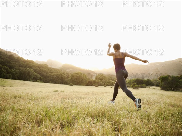 Mixed race woman running through remote field