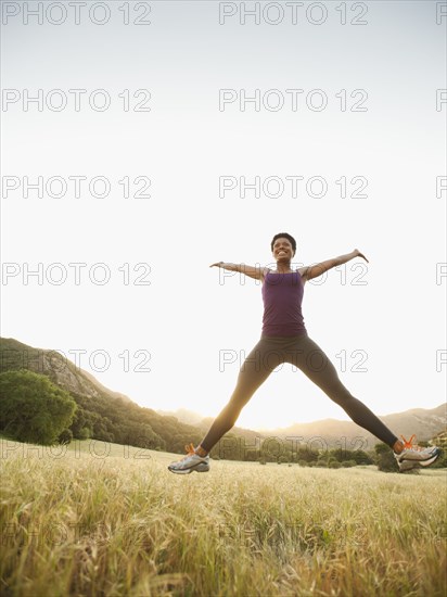 Mixed race woman jumping in remote field