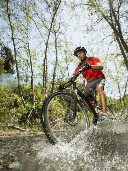 Mixed race man riding mountain bike through stream