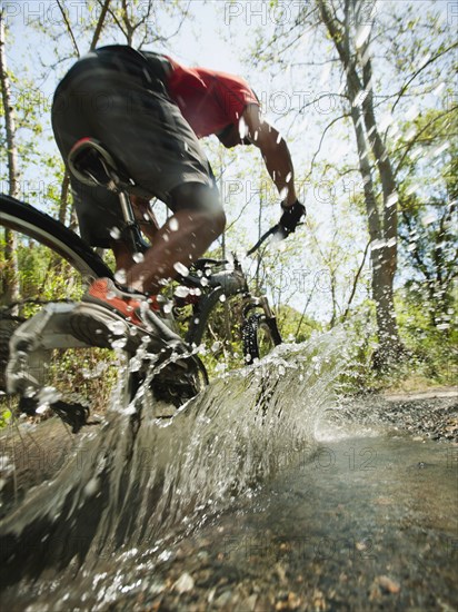 Mixed race man riding mountain bike through stream