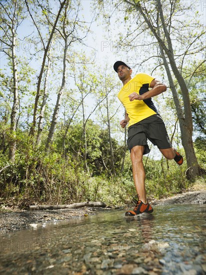 Mixed race man running through stream