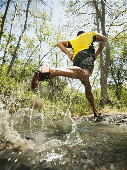 Mixed race man running through stream