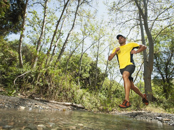 Mixed race man running through stream