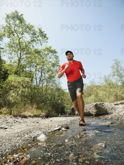 Mixed race man running through stream