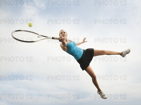 Caucasian woman jumping in mid-air playing tennis