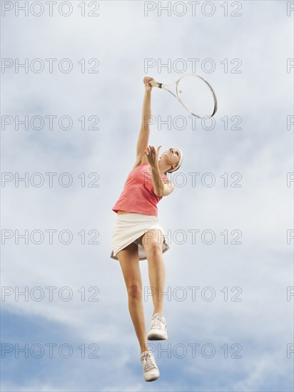 Caucasian woman jumping in mid-air playing tennis