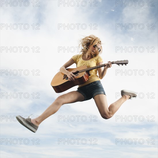 Caucasian woman jumping in mid-air playing guitar