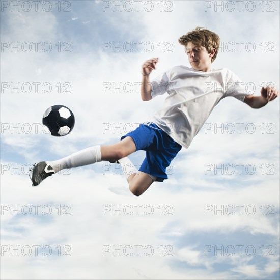 Caucasian teenager kicking soccer ball in mid-air