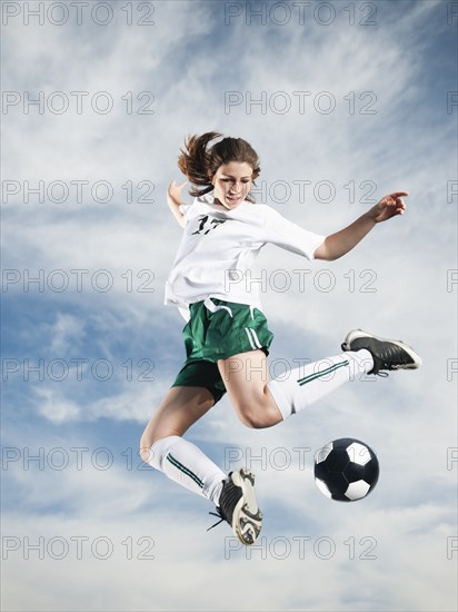 Caucasian teenager kicking soccer ball in mid-air