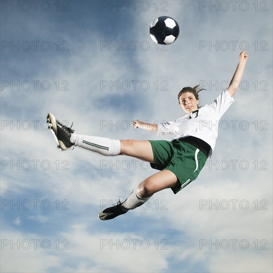 Caucasian teenager kicking soccer ball in mid-air