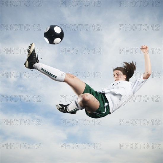 Caucasian teenager kicking soccer ball in mid-air