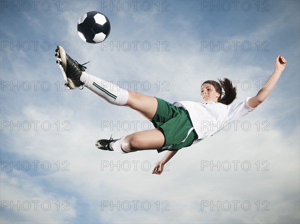 Caucasian teenager kicking soccer ball in mid-air