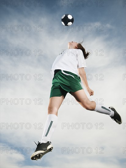 Caucasian teenager heading soccer ball in mid-air