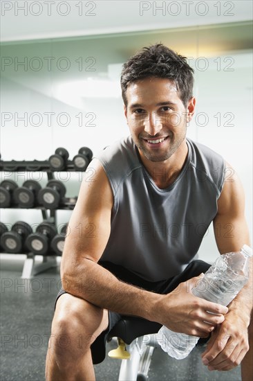 Mixed race man drinking water in gym