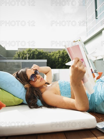 Mixed race woman sunbathing and reading magazine