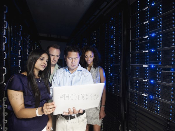 Business people looking at laptop in server room