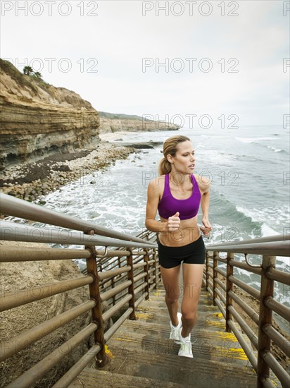 Caucasian woman running up stairs next to ocean