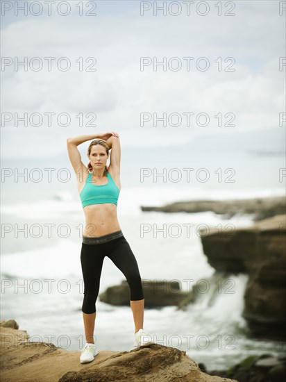 Caucasian woman stretching on rocks near ocean