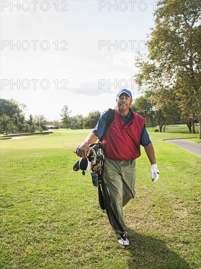 Black man carrying golf clubs