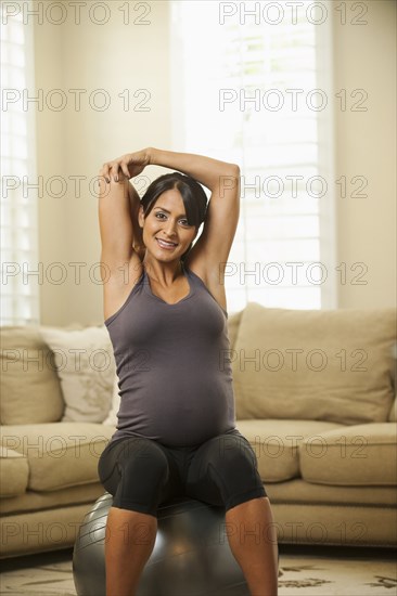 Pregnant Hispanic woman stretching on exercise ball