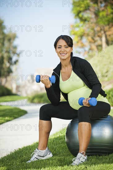 Pregnant Hispanic woman lifting weights outdoors