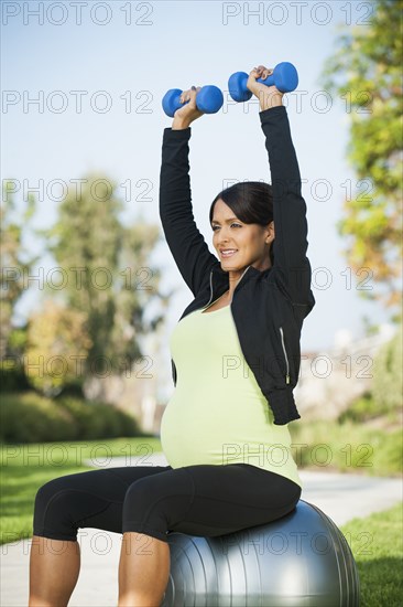 Pregnant Hispanic woman lifting weights outdoors