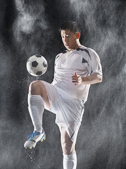 Asian soccer player kicking ball in rain