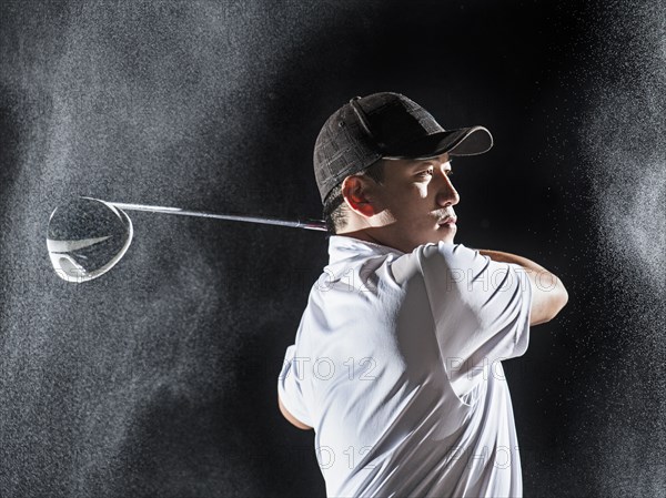 Asian golf player swinging club in rain