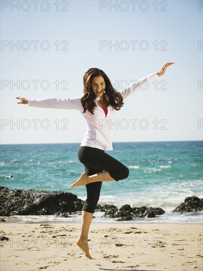 Mixed race woman jumping for joy on beach