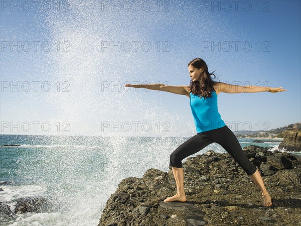 Mixed race woman practicing yoga on rocky beach