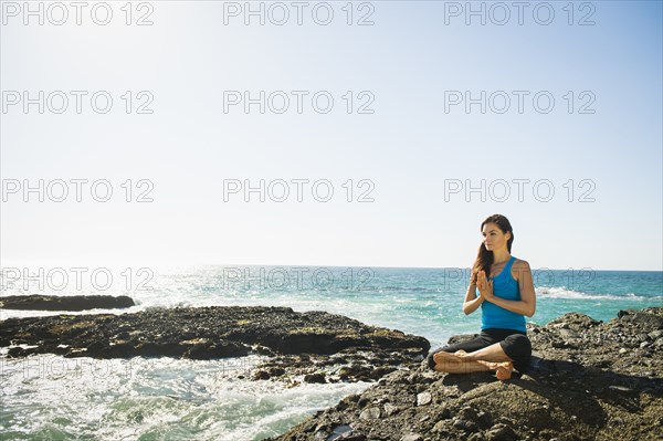 Mixed race woman meditating on rocky beach