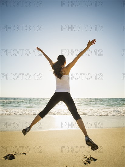 Mixed race woman jumping for joy on beach